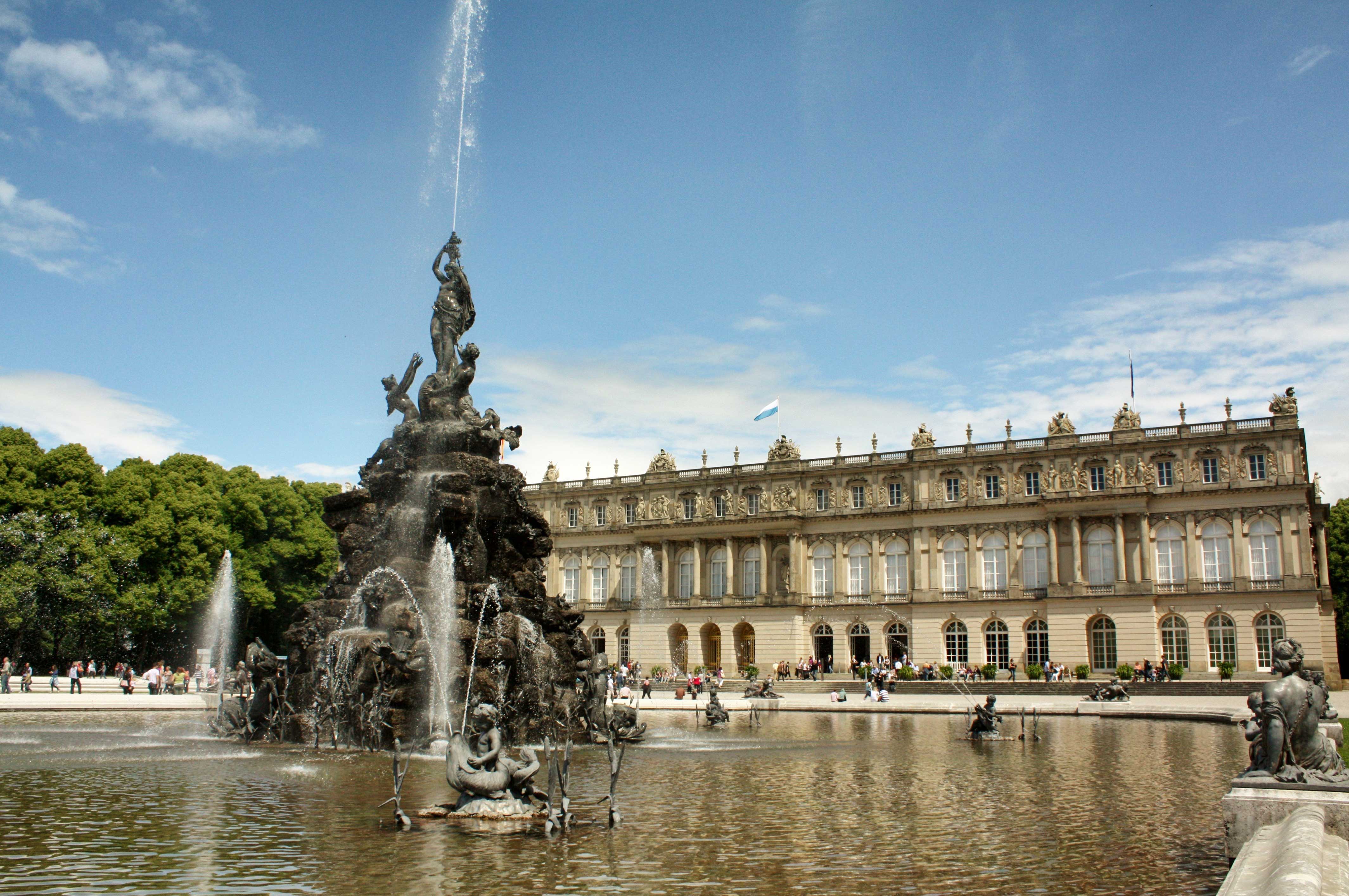 a fountain with a large building in the background with Herrenchiemsee in the background